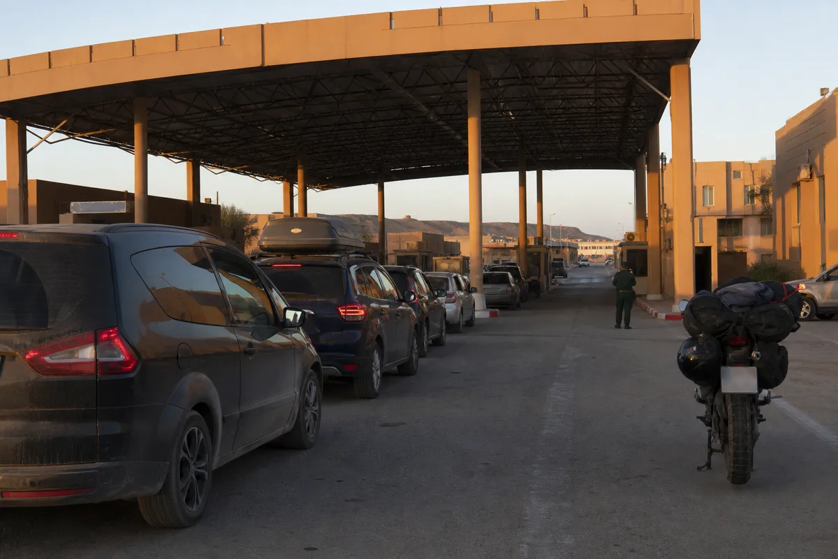 Poste frontière routier marocain avec plusieurs véhicules et une moto garés en file sous un auvent