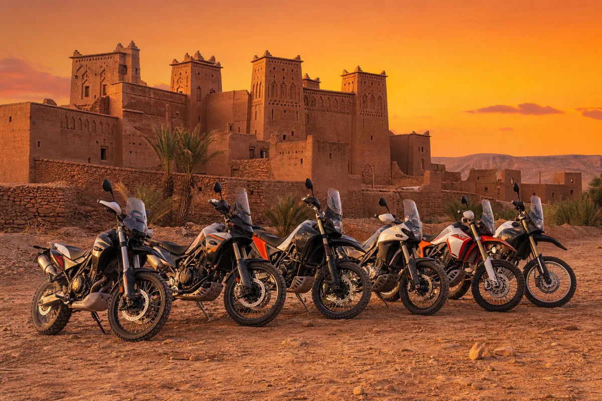 Plusieurs motos de type trail garées côte à côte devant une kasbah en pisé ocre au coucher du soleil